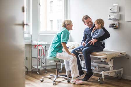 Sjuksköterska som pratar med ett barn som sitter i pappas knä