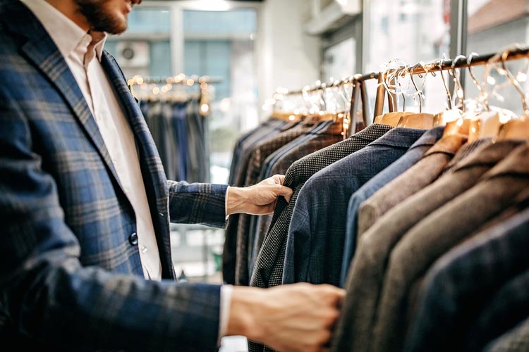 En man i kavaj står i en klädbutik och granskar ett urval av upphängda kavajer på en klädställning